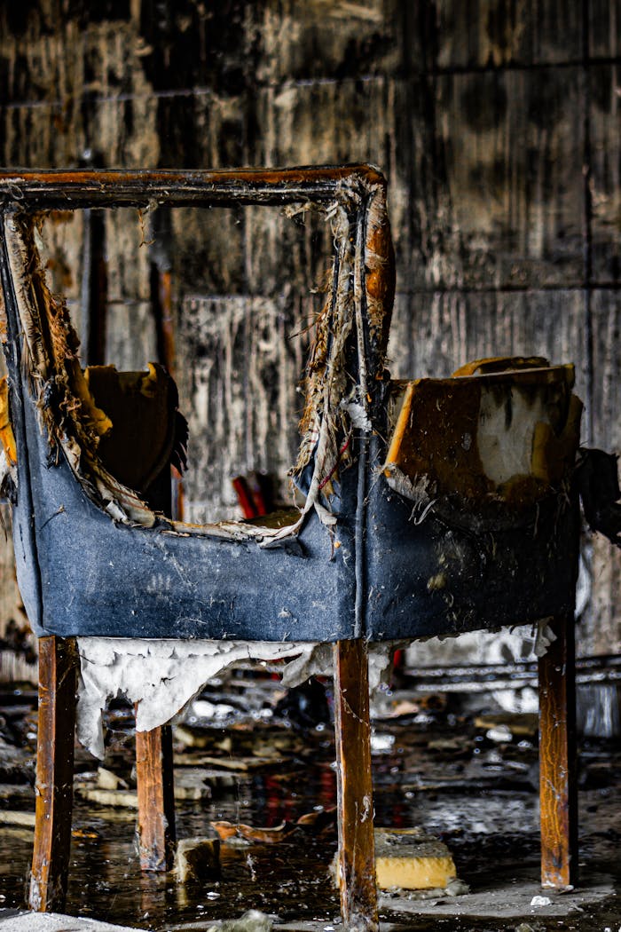 A worn, burnt chair in an old, abandoned room with peeling walls.