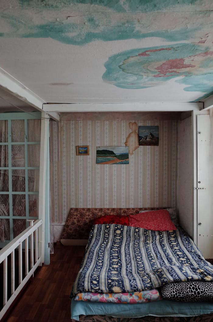 A small bedroom with a unique ceiling design, featuring water stains and an eclectic bed setup.